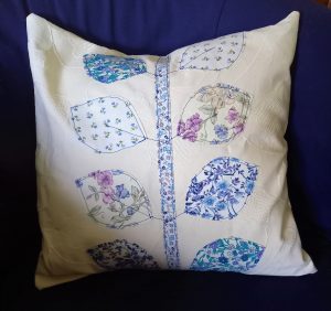 White cushion with applique leaves, mixed floral patterns
