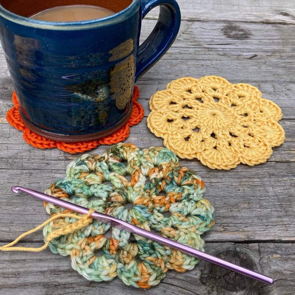 Three crocheted coasters with a crochet hook and blue mug of tea